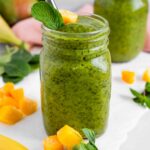 A mango mint green smoothie in a mason jar with a stainless steel straw.