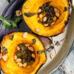 Two roasted and caramelized acorn squash halves are sprinkled with sage and roasted squash seeds.