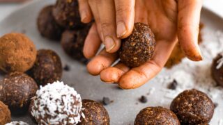 Hands roll a no bake energy ball. Some brownie flavoured energy balls are rolled in coconut or cocoa powder.