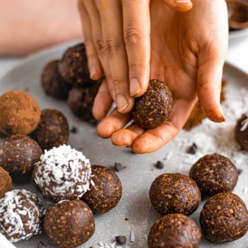 Hands roll a no bake energy ball. Some brownie flavoured energy balls are rolled in coconut or cocoa powder.