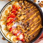 Top down view of a chocolate smoothie bowl topped with banana and strawberry slices and drizzled with peanut butter.