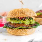 A portobello mushroom burger with avocado and chimichurri between a sesame seed bun.