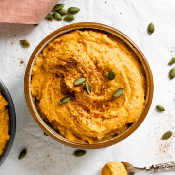 Top down view of creamy pumpkin hummus filling a small bowl garnished with pumpkin seeds.
