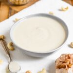 Side view of roasted garlic cashew cream sauce filling a small dish. A bulb of roasted garlic sits next to the cream.