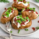Vegan baked potatoes loaded with sour cream, sun-dried tomato bits, and sliced green onion.