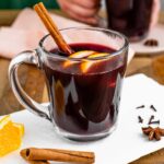 Side view of a mug of mulled wine garnished with orange slices and a cinnamon stick.