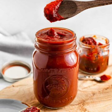 Easy chipotle BBQ sauce fills a mason jar. A wooden spoon scoops the deep red, thick, and spicy sauce.