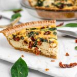 Side view of a sturdy slice of vegan quiche with spinach and sun-dried tomatoes.