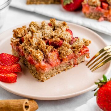Side view of a vegan strawberry crisp bar on a plate. The topping is golden brown and dusted with cinnamon.