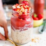 A mason jar filled with overnight oats topped with strawberry jam and sprinkled with toasted almonds.