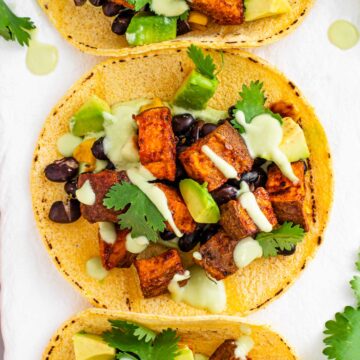 Top down view of a roasted sweet potato taco on a corn tortilla with black beans, avocado, and a creamy avocado dressing.