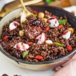 A spoon lifts up from an elegant vegan chocolate mousse dessert. Cherry sauce and a toasted hazelnut and oat crumble sit atop the mousse.