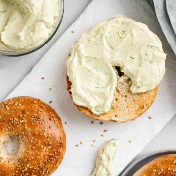 Top down view of thick vegan cream cheese spread on half of a toasted sesame bagel.