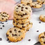 A tower of vegan chocolate chip cookies on a white tray with chocolate chips scattered around.