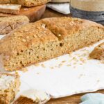 Side view of a loaf of vegan Irish soda bread sliced in half. It's golden brown and the top is sprinkled with oats.