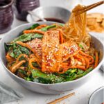 Side view of sweet potato noodles being lifted from a bowl of vegan Japchae topped with tofu strips.