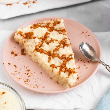 A pie shaped slice of Portuguese sweet rice sits on a small plate. A criss cross pattern of cinnamon garnishes the vegan arroz doce.