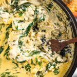 Top down view of creamy spinach artichoke dip in a cast iron skillet. A spoon digs into the warm dip.