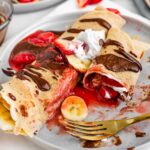 Side view of a plate of crepes with one crepe half eaten exposing the warm strawberry filling.