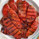 Top down view of watermelon steaks on a serving plate with grill lines seared into the fruit.