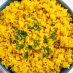 Top down view of yellow turmeric rice filling a serving bowl and garnished with fresh cilantro.