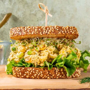 Side view of chickpea smash on a bed of lettuce and topped with sprouts between two pieces of seeded bread.