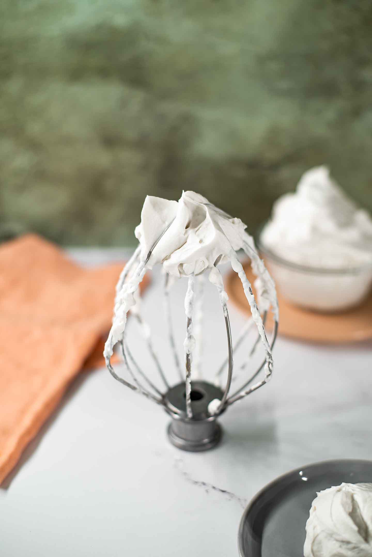 Close up of fluffy coconut whipped cream swirled on the whisk attachment of a stand mixer. The whip is firm enough that it holds its shape and stays firm on the upright whisk.