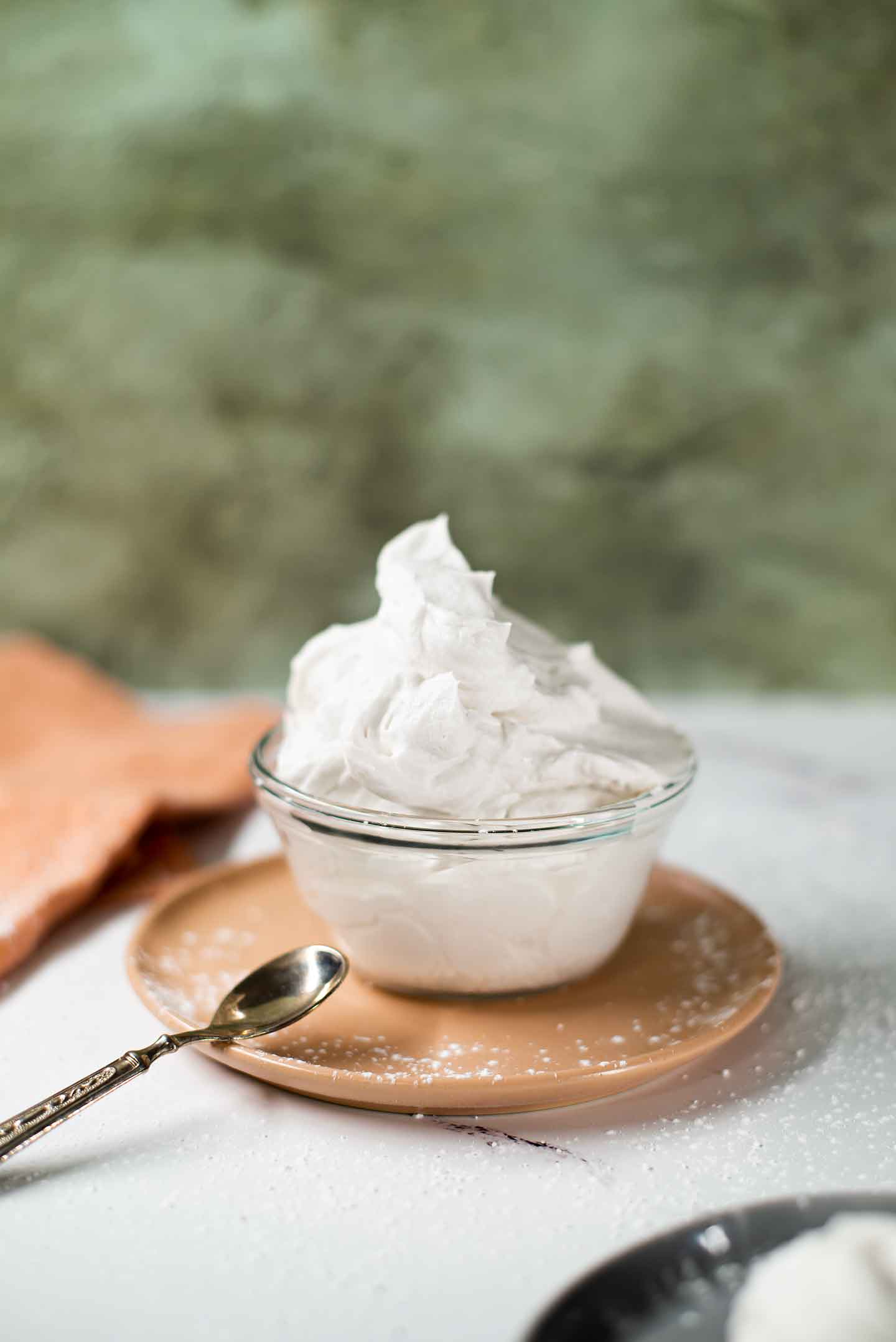 Close up of fluffy coconut whipped cream in a small glass bowl. The whipped cream billows like fluffy clouds up from the bowl.