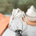 Fluffy coconut whipped cream swirls up from the top of a whisk attachment from a stand mixer. The whipped cream is firm enough that it holds its shape and doesn't fall.