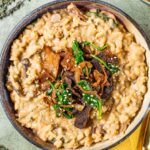 Top down view of creamy risotto in a dish topped with wild mushrooms, caramelized onion, and wilted spinach.