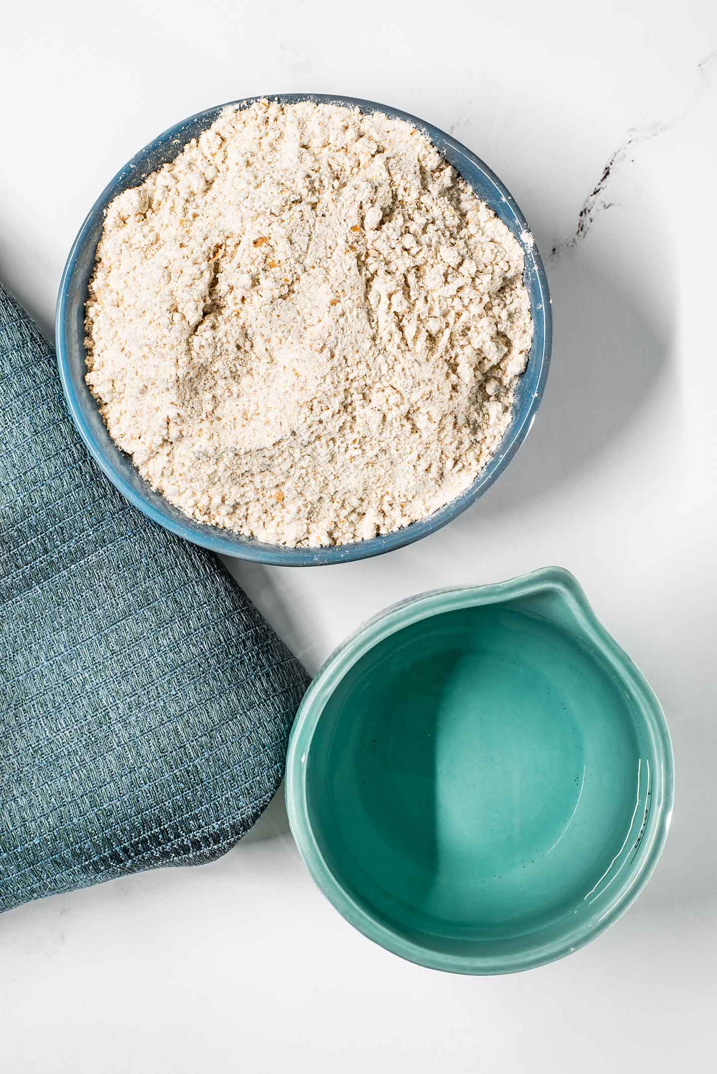 Top down view of whole wheat flour in a dish and a measuring cup of water.
