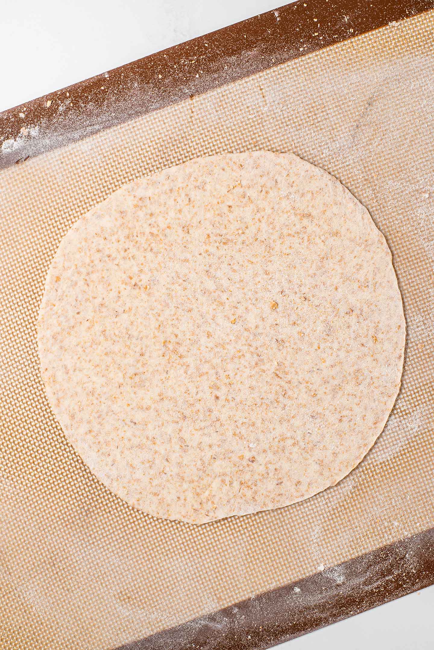 Top down view of roti dough rolled into the thin circular shape before being cooked.