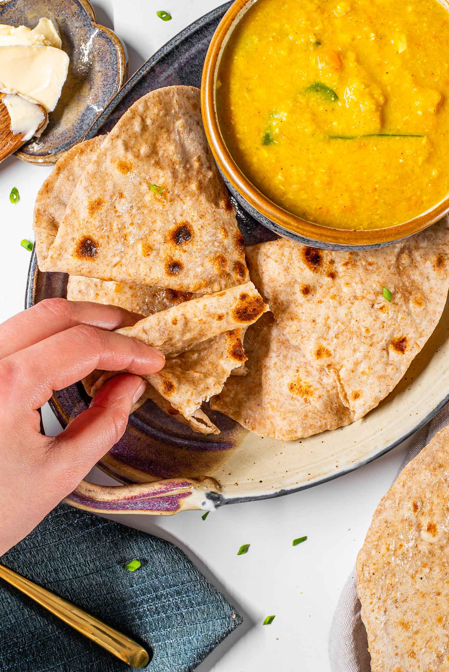 Top down view of a hand folding roti and preparing to dip it into a bowl of dal.