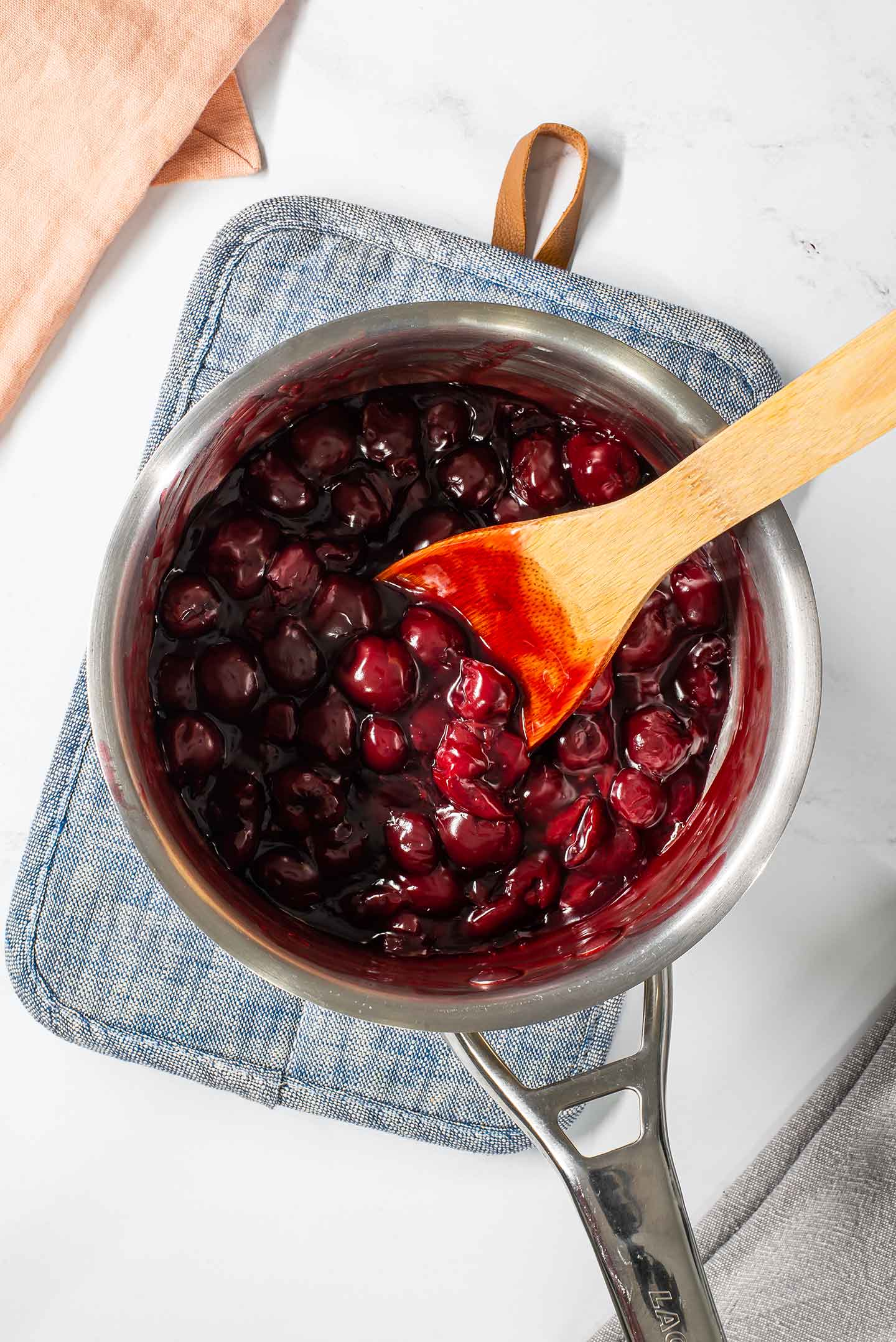 Top down view of a thick cherry filling in a small pot. A wooden spoon rests in the cherries.