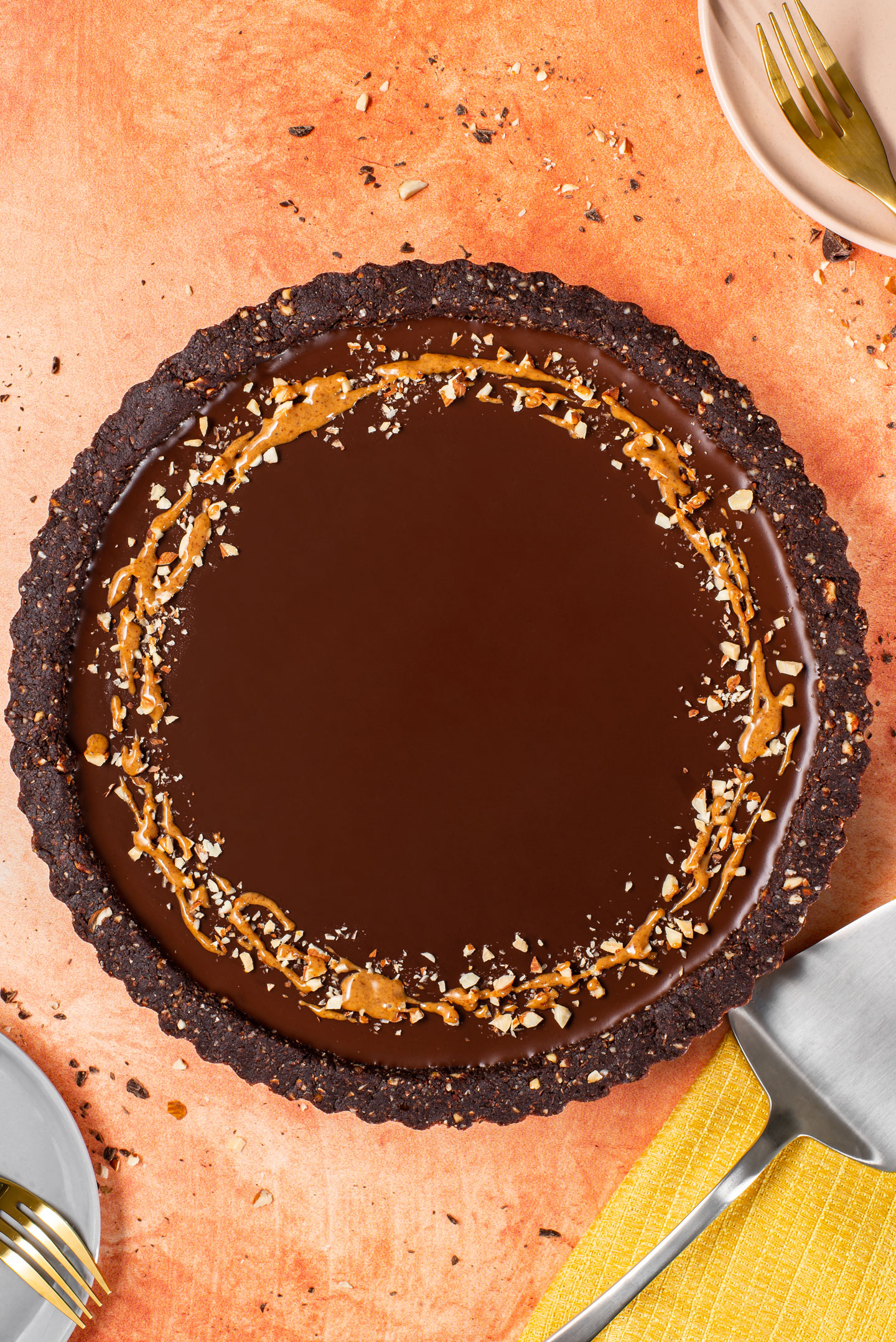 Top down view of a vegan chocolate tart. The dark chocolate tart is delicately decorated with crushed toasted almonds and an almond butter drizzle.