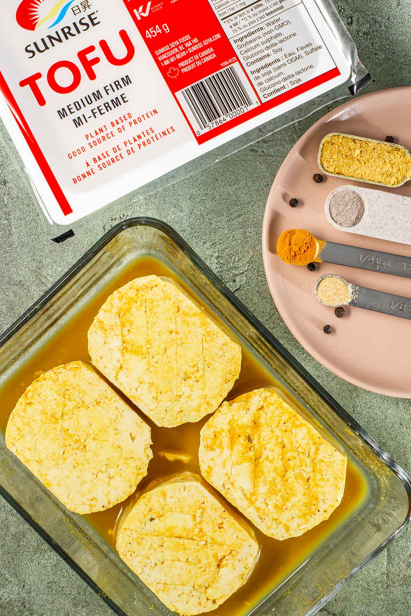 Top down view of four tofu eggs marinating in a turmeric sauce. A package of medium firm tofu is also pictured.