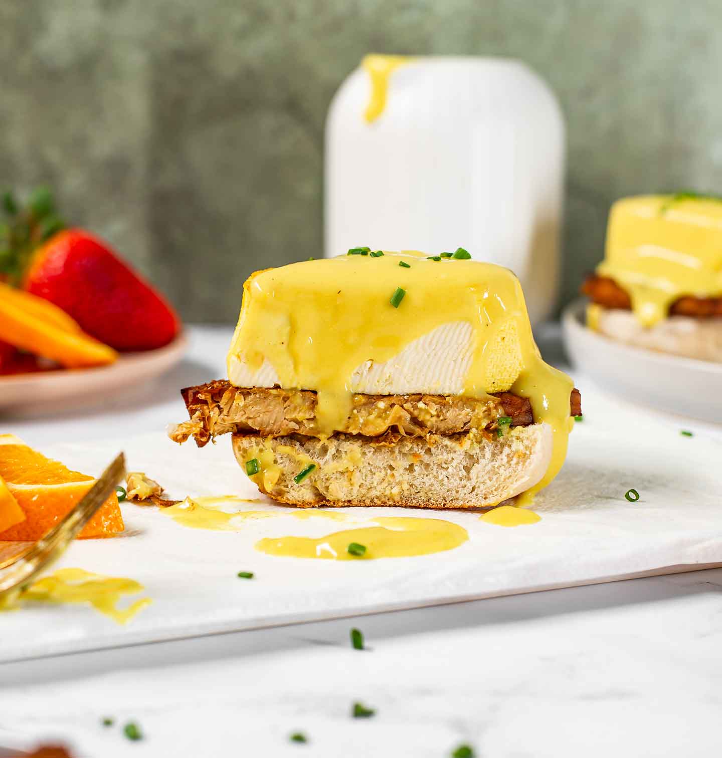 Side view of a vegan eggs benedict sliced through the middle. Creamy vegan hollandaise sauce drips down the tofu egg.