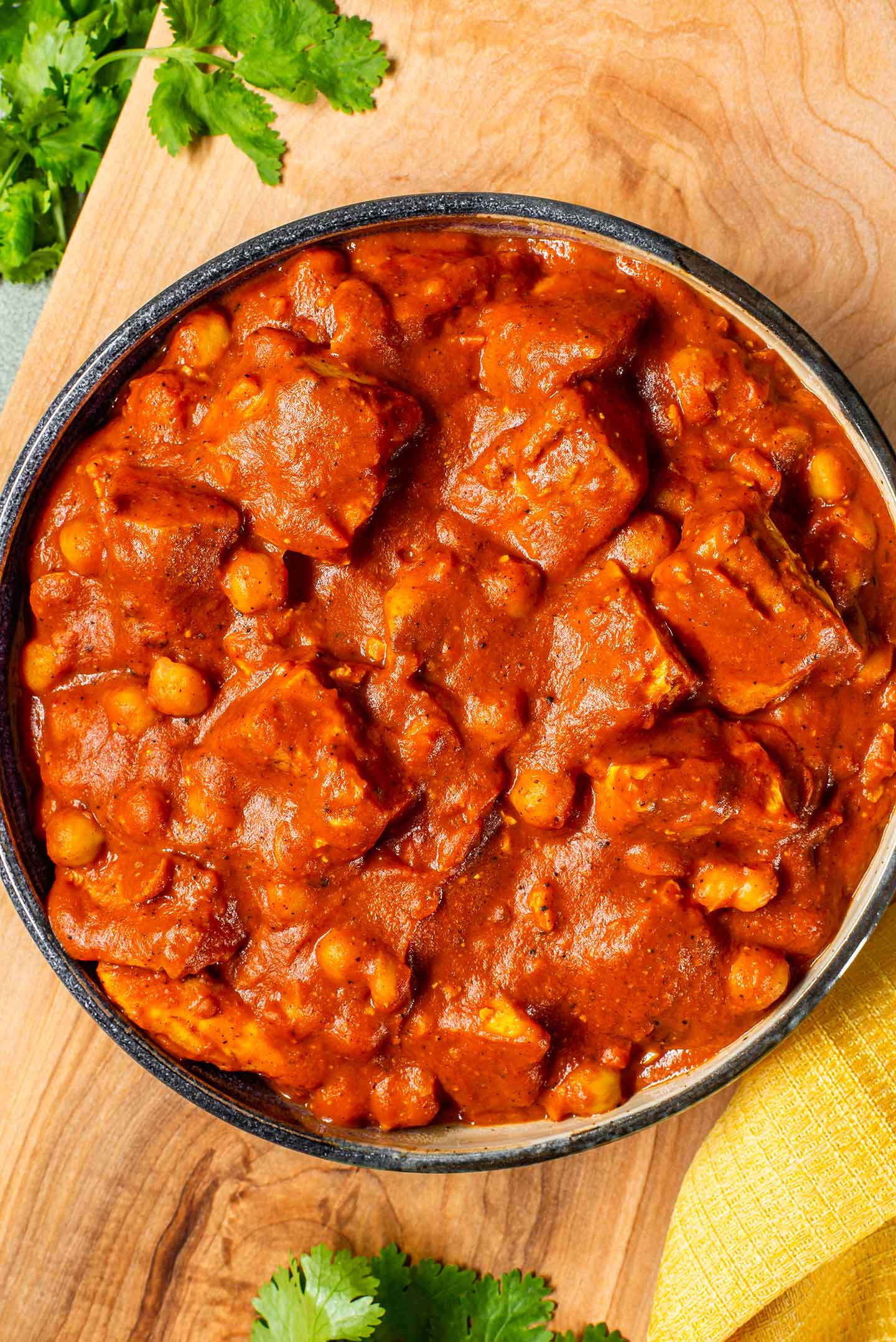 Top down view of a bowl full of thick and creamy vegan butter chicken. The sauce is reddish brown and coating chunks of tofu and chickpeas.