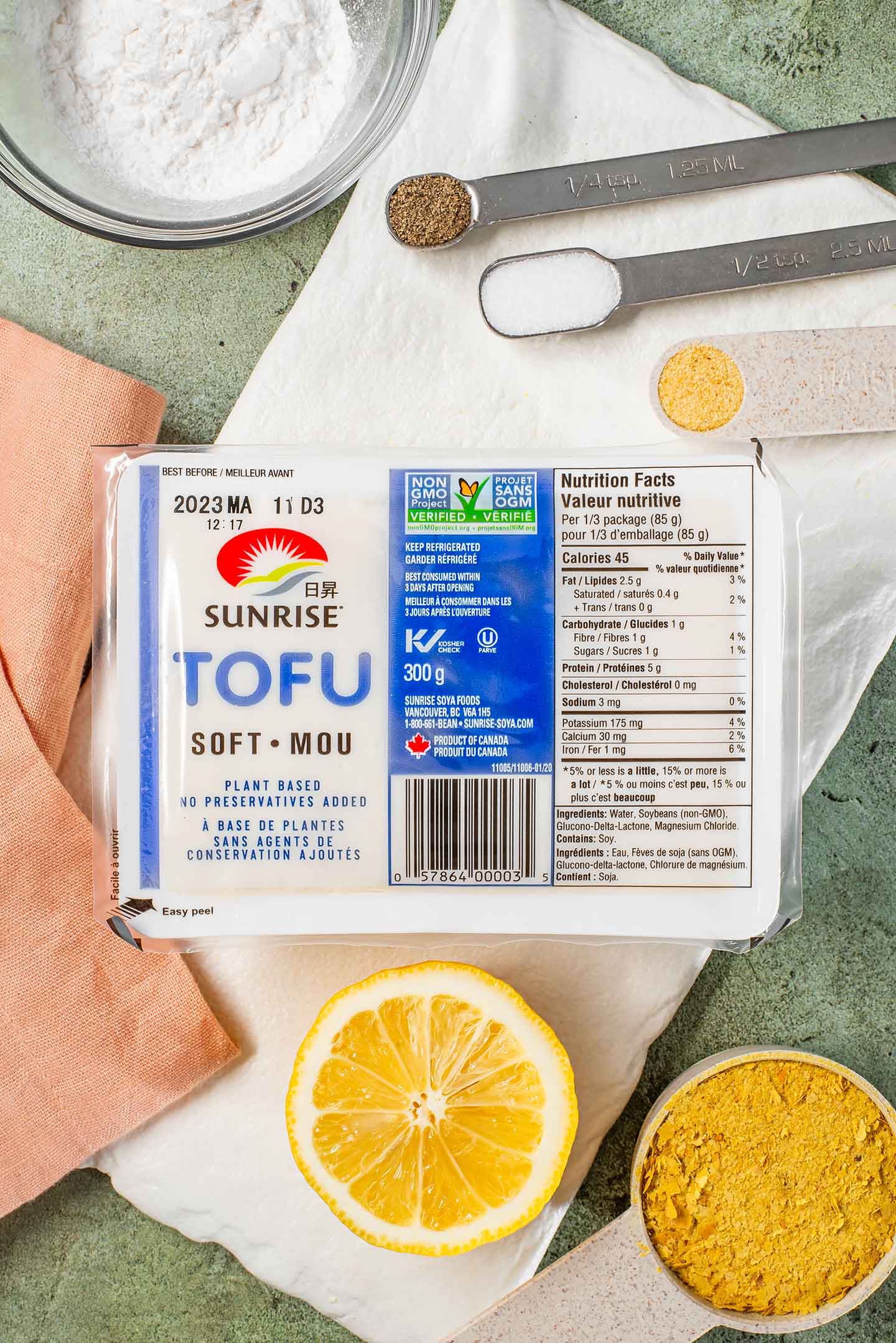 A package of silken or soft tofu is surrounded by a cut lemon, tapioca starch, and seasonings.