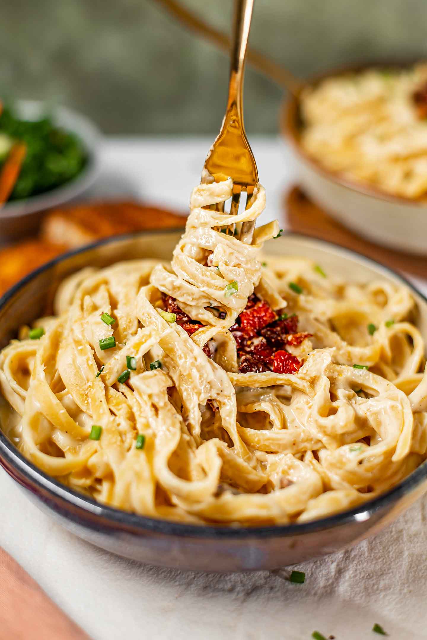 Side view of fettuccine noodles wrapped around a fork and lifting up from a bowl of creamy dairy-free fettuccine alfredo.