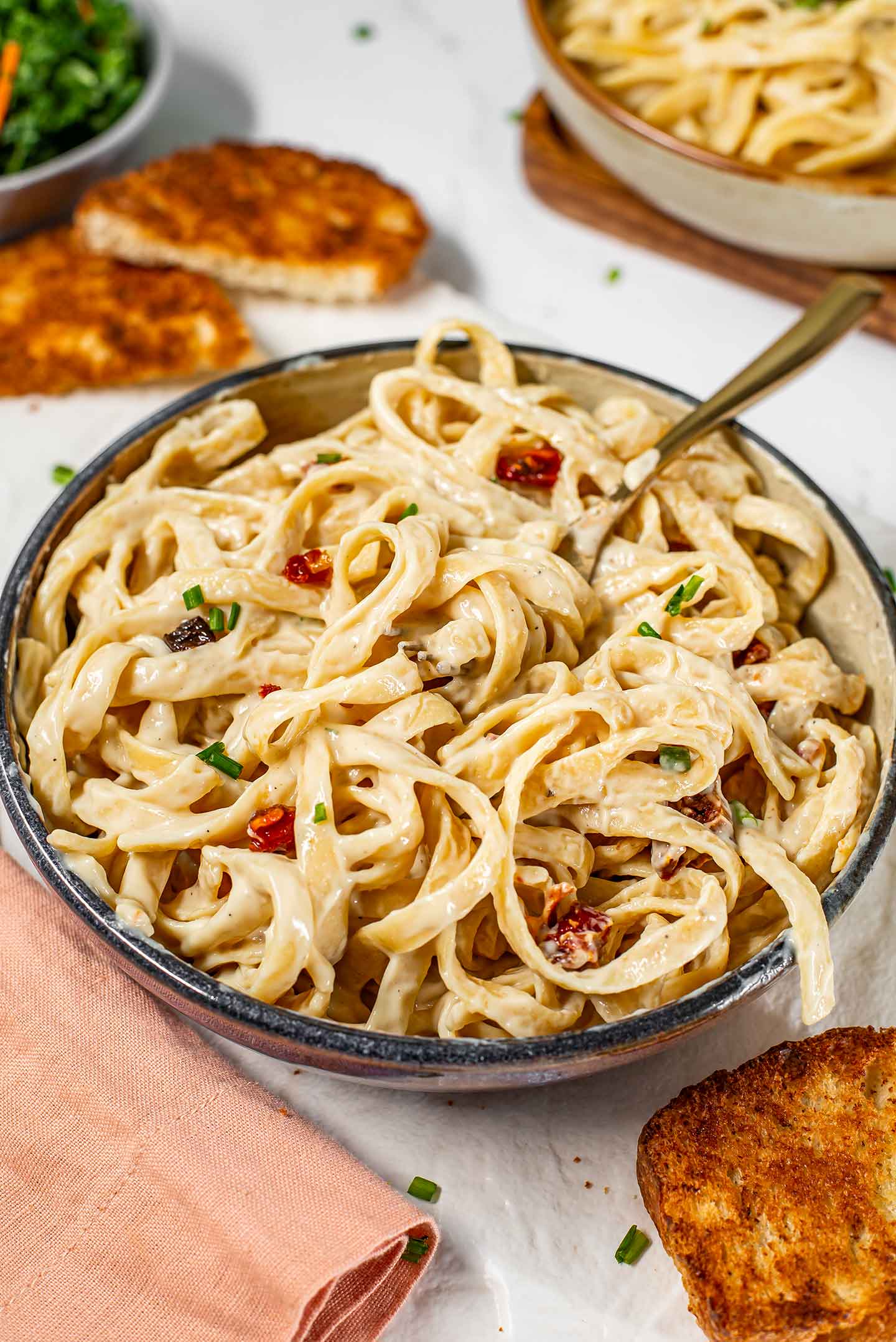 A fork rests in a bowl of dairy-free fettuccine alfredo. The creamy noodles spill over the sides of the pasta bowl.