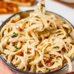 Fettuccine noodles covered in a creamy vegan alfredo sauce spill over the sides of a bowl.