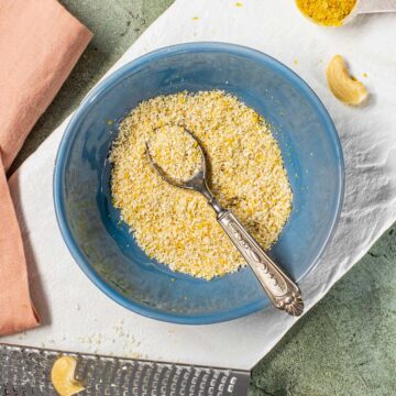 Top down view of a vegan parmesan cheese topping in a bowl. The topping is made of shaved cashews, nutritional yeast, and salt.