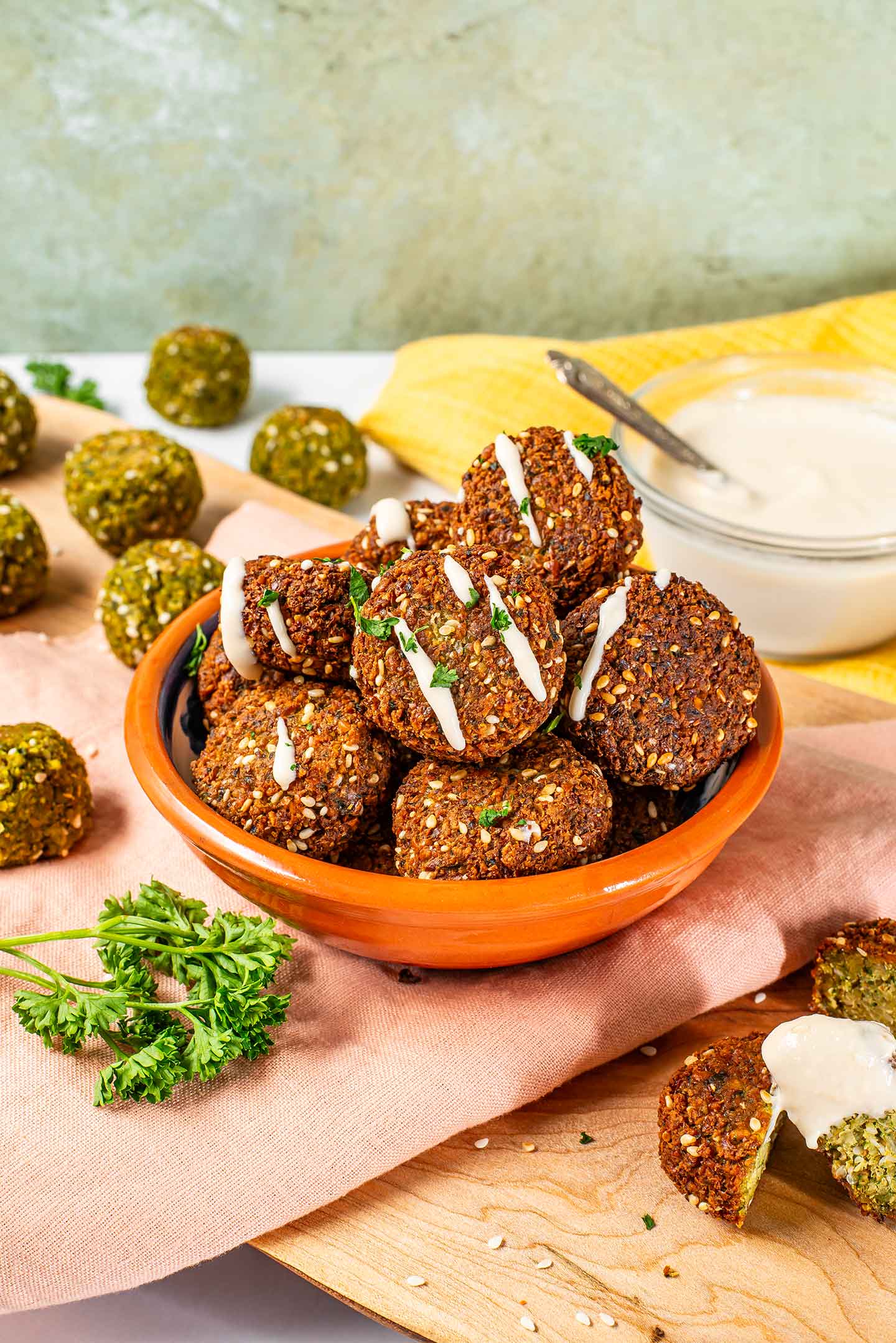 Side view of falafel in a small bowl drizzled with a lemon tahini dressing and sprinkled with parsley.
