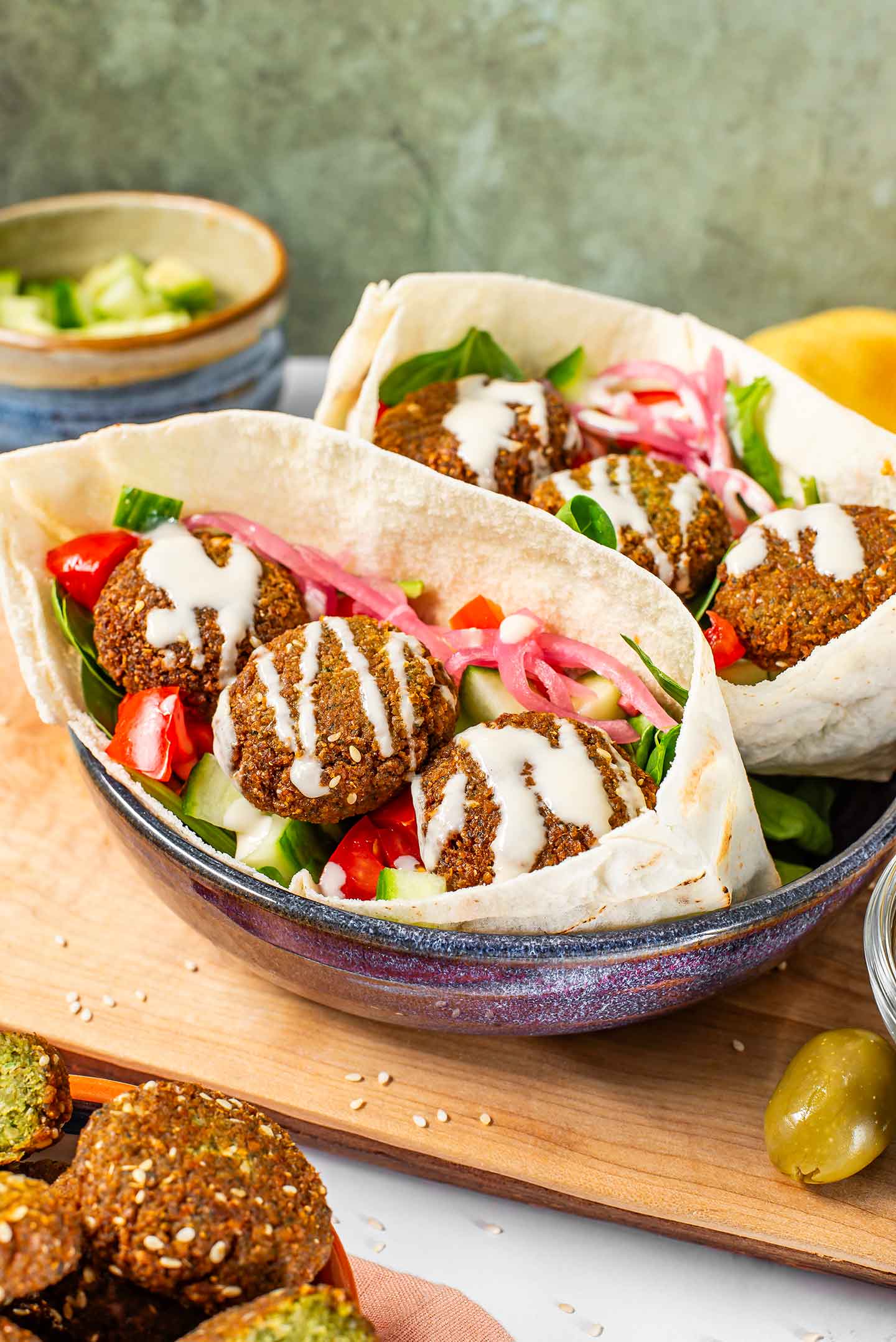 Crispy falafel sit atop a bed of spinach, tomato and cucumber in two halves of a pita pocket. A creamy tahini dressing is drizzled over the fillings.
