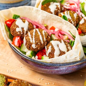Three crispy falafel sit atop a bed of spinach, tomato and cucumber in a pita pocket. A creamy tahini dressing is drizzled inside.