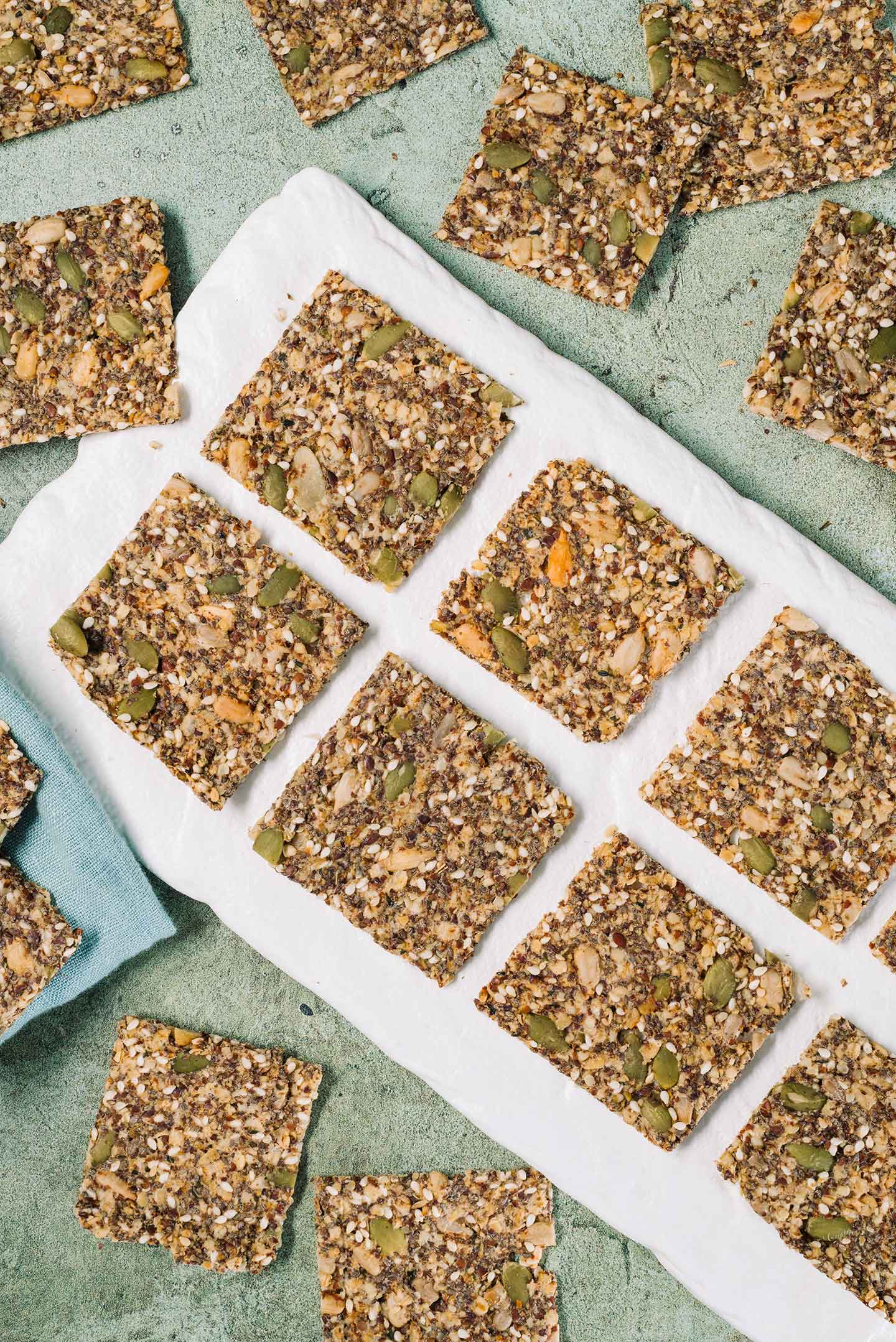Top down view of gluten-free seed crackers arranged on a white tray. The square crackers look thin and crispy.