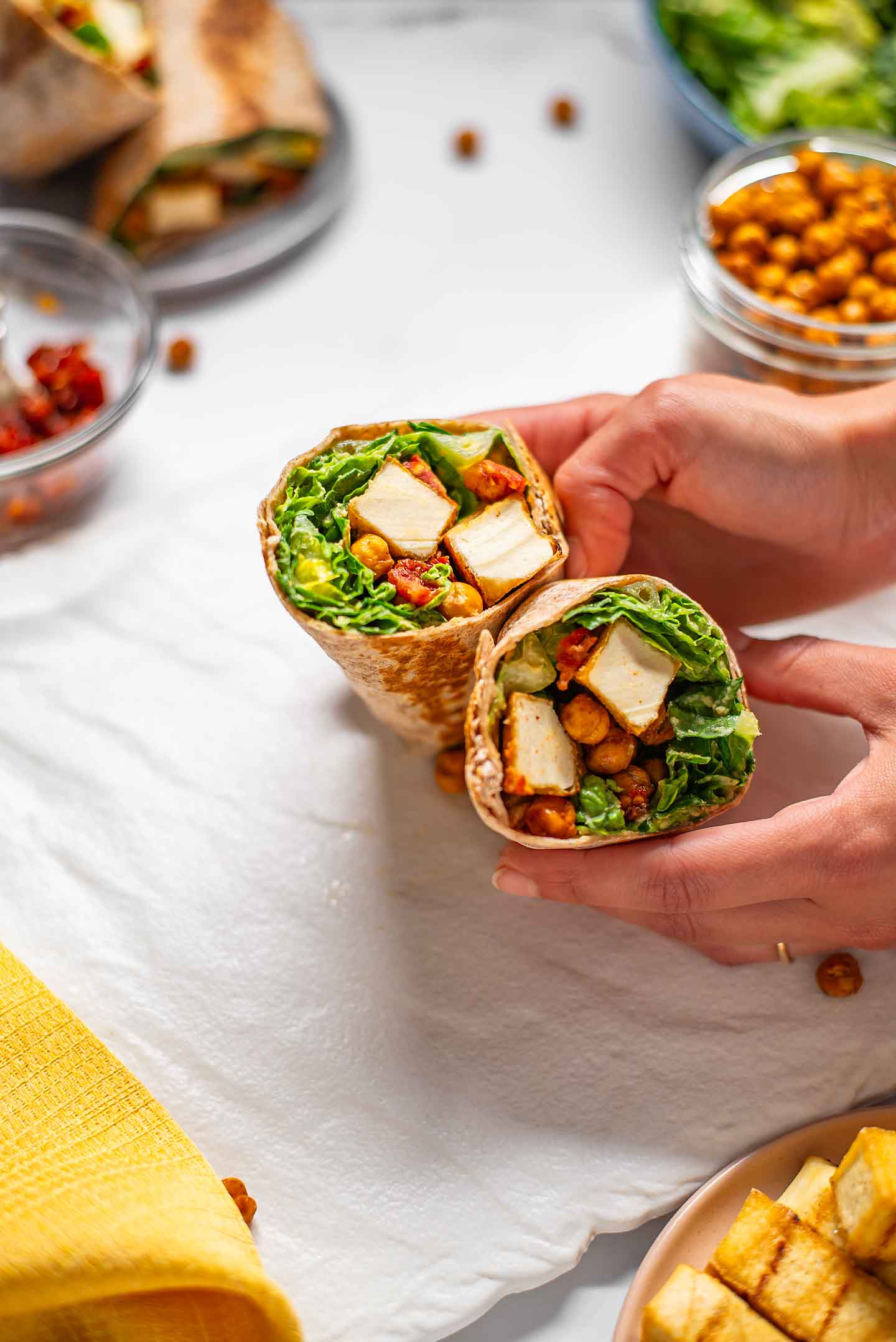 Top down view of hands holding a sliced vegan caesar wrap to show its contents.