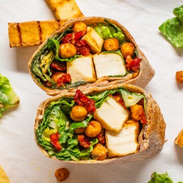 Top down view of a vegan caesar wrap cut in half and exposing strips of grilled tofu, romaine lettuce with vegan caesar dressing, roasted chickpeas, and sun-dried tomato "bacon bits".
