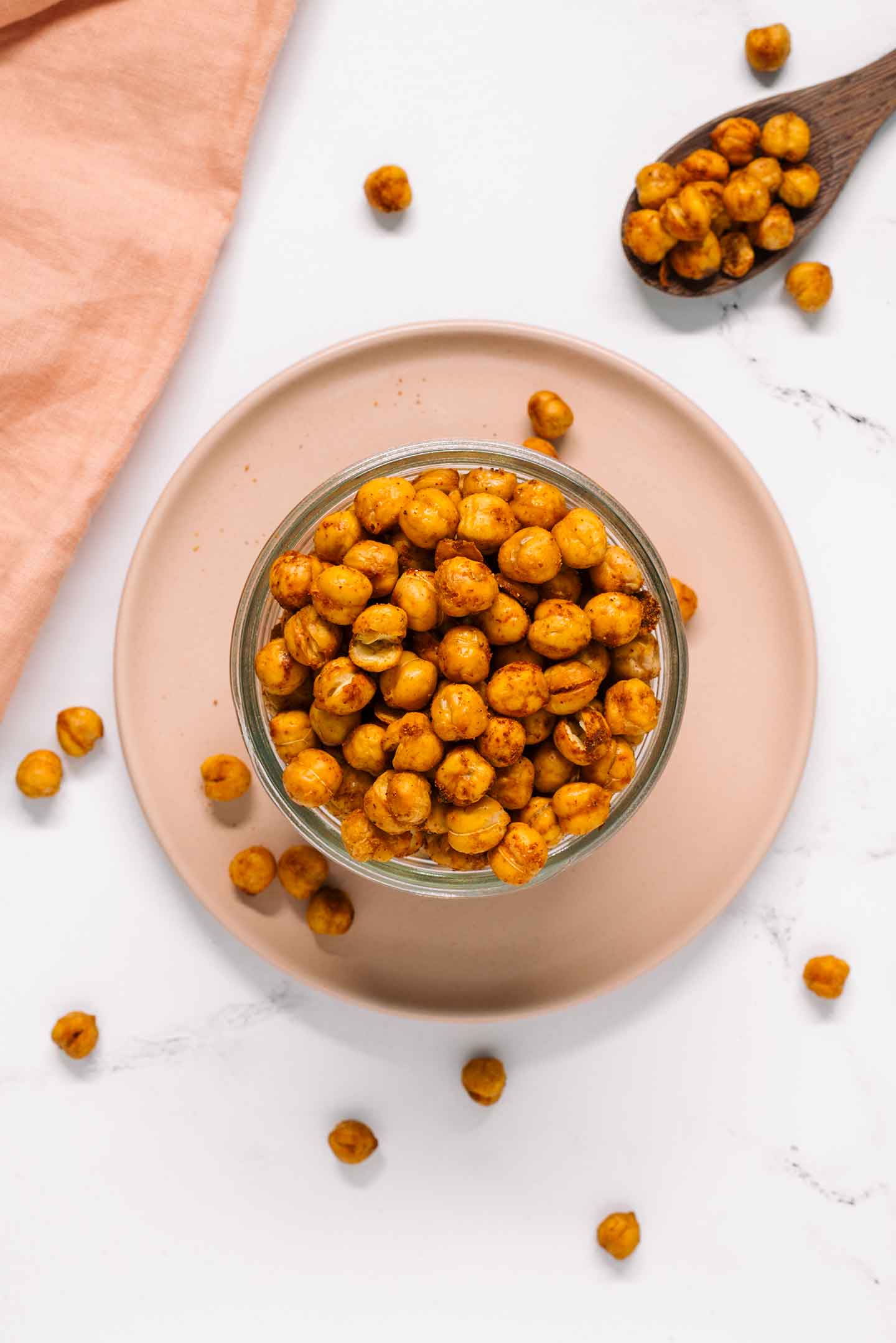 Top down view of lightly seasoned crunchy roasted chickpeas in a small bowl. A spoon rests nearby with crunchy chickpeas spilling from it.